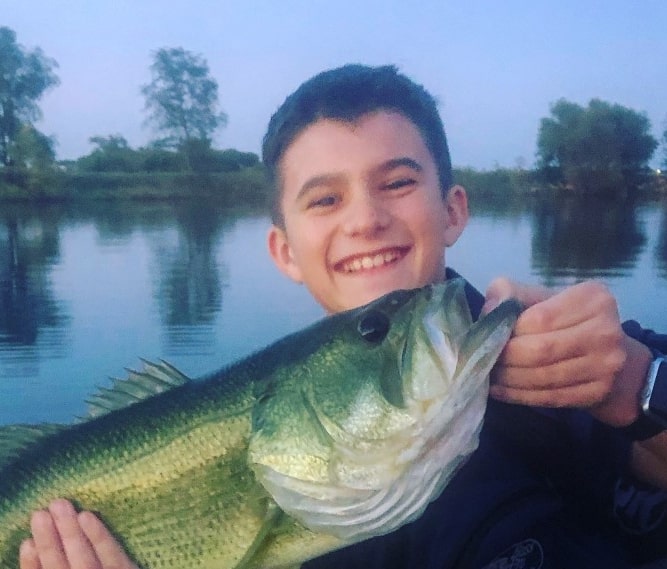 Young male boy holding Bass fish caught while fishing in lake